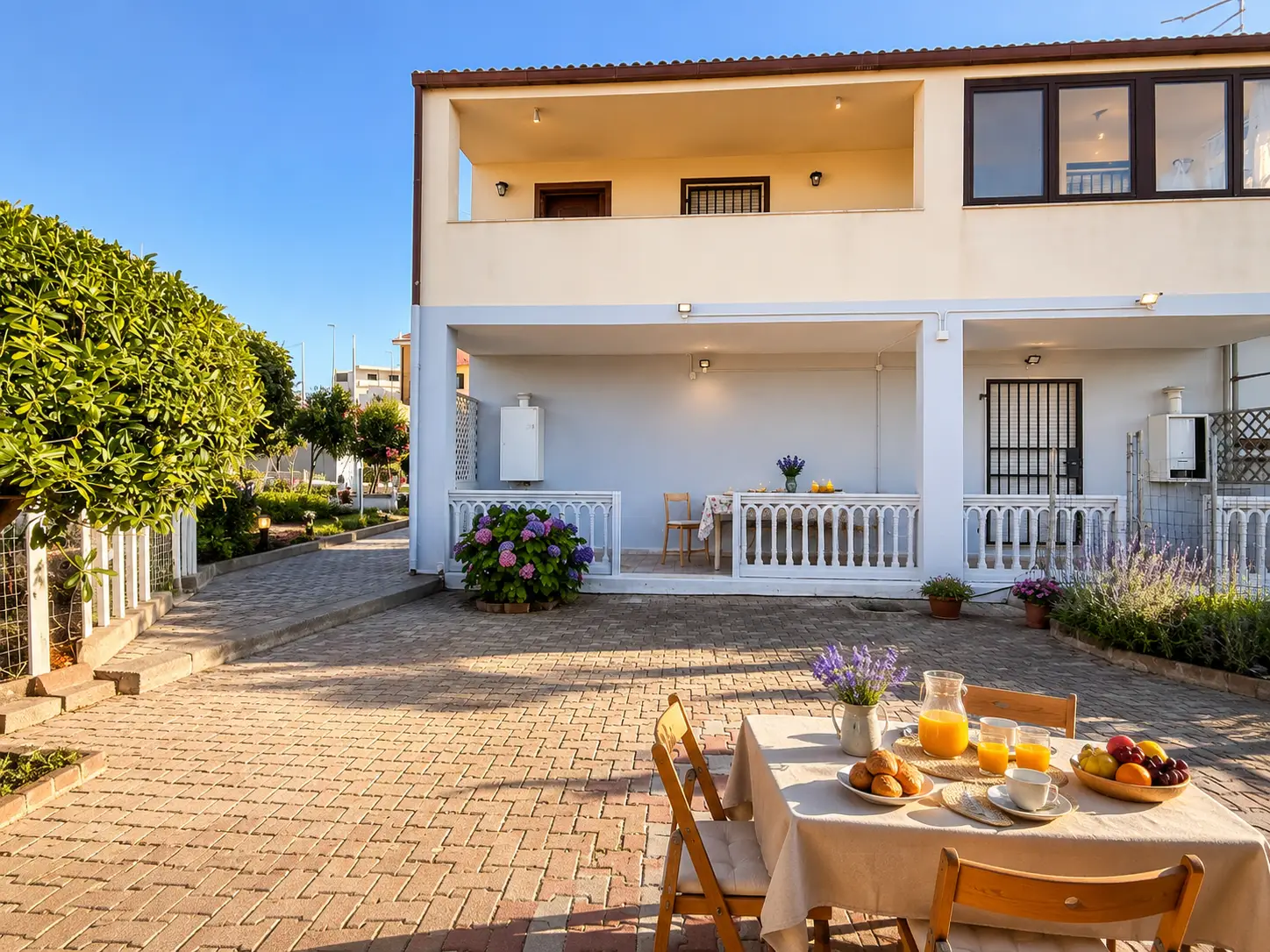 Facciata di una casa vacanze con ampio cortile pavimentato e tavolo apparecchiato per la colazione all'aperto.